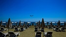 Einige Menschen sonnen sich am Makenzi Strand auf Zypern, während sich im Hintergrund ein Flugzeug auf die Landung am internationalen Flughafen Larnaca vorbereitet.  | Bild: dpa-Bildfunk/Petros Karadjias