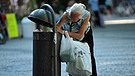 In einem Mülleimer auf einem größeren Platz sucht eine ältere Frau nach Pfandflaschen.  | Bild: picture-alliance/dpa