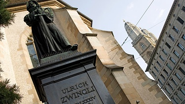Denkmal von Ulrich Zwingli vor der Wasserkirche, hinten das Grossmünster in Zürich  | Bild: picture alliance_imageBROKER_Meinrad Riedo.jpg