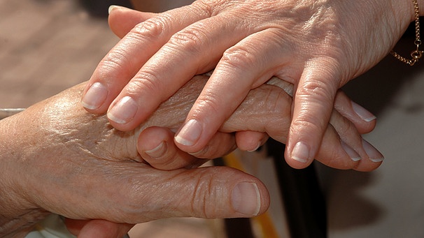Eine Betreuerin streichelt während des "Betreuten Urlaubs" für Alzheimerkranke einer Patientin die Hand. | Bild: picture-alliance/dpa