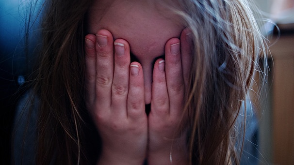 Mädchen verbirgt sein Gesicht vor Kummer hinter den Händen. | Bild: picture-alliance/dpa