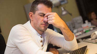 Junger Mann, sichtlich gestresst am Arbeitsplatz | Bild: picture-alliance/dpa