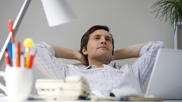 Entspannen im Büro - im Bild: Mann entspannt sich am Schreibtisch mit verschrenkten Armen hinter dem Kopf | Bild: colourbox.com