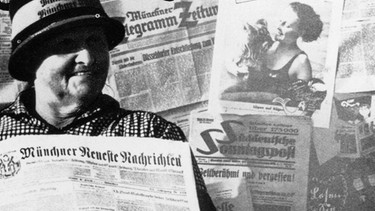 Zu sehen ist eine ältere Dame, die eine Zeitung in der Hand hält; hinter und vor ihr sind ebenfalls Zeitungen drapiert. Es handelt sich um ein altes schwarz-weiß Foto. | Bild: picture-alliance akg-images