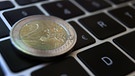 Eine Zwei -Euro-Münze liegt auf der Tastatur eines Laptops neben einem Eurozeichen.
| Bild: picture alliance/dpa | Karl-Josef Hildenbrand