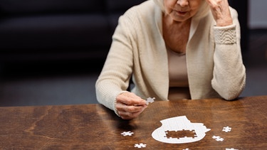 Eine Frau sitzt vor einem Puzzle in Form eines Kopfes.  | Bild: colourbox.com