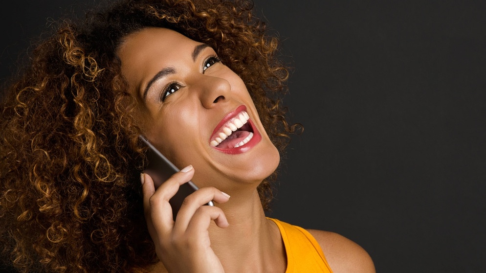 Eine Frau spricht und lacht am Telefon | Bild: picture-alliance/dpa