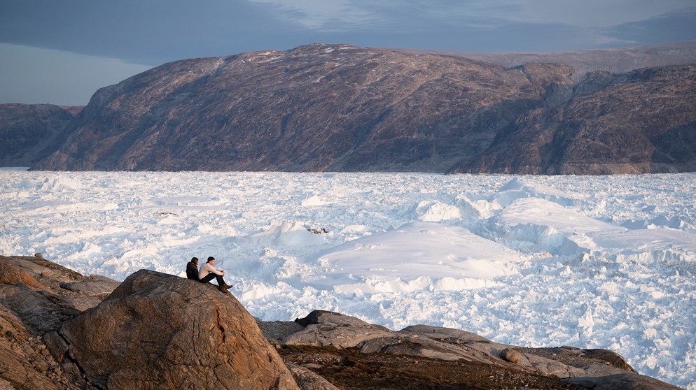 2019, Grönland, Helheim Glacier: Zwei Studenten der New York University, sitzen auf einem Felsen mit Blick auf den Helheim-Gletscher. | Bild: dpa-Bildfunk