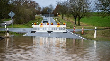 Ein Auto fährt auf eine Straße zu, die wegen Überschwemmung gesperrt ist. Die Itz führt Hochwasser, etliche Straßen sind gesperrt. (Vom 04.01.2024) | Bild: picture alliance/dpa | Pia Bayer