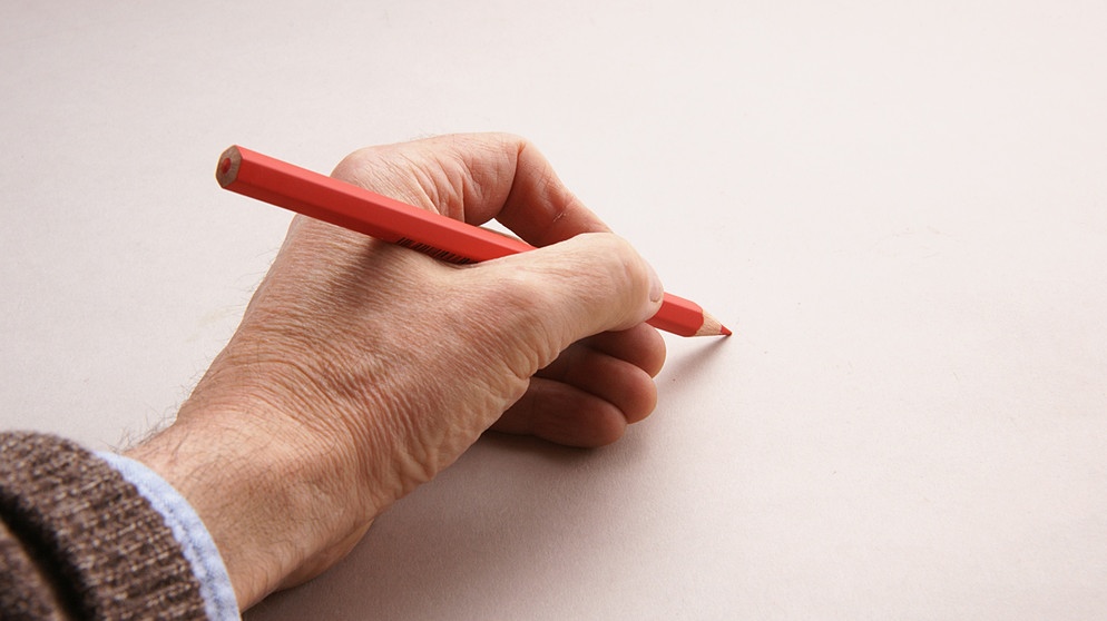 Eine linke Hand hält einen Stift an ein Blatt Papier. | Bild: BR/Thomas Schmidt