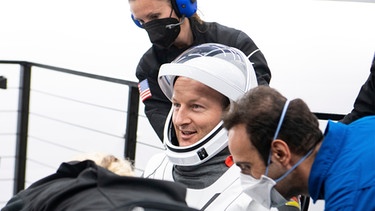 Astronaut mit geöffnetem Helm des Raumanzuges wird nach der Landung von der Raumstation in Empfang genommen | Bild: picture-alliance/dpa