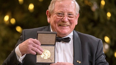 Reinhard Genzel, deutscher Physiker, hält bei der Übergabe des Nobelpreises für Physik die goldene Medaille in seinen Händen.  | Bild: picture-alliance/dpa