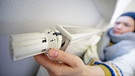Symbolbild zum Thema "Heizkosten sparen". Eine Frau mit Mütze und Schal dreht am Thermostat eines Heizkörpers. | Bild: picture-alliance/dpa