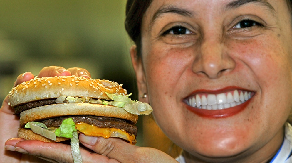 Eine Mitarbeiterin der Fastfood-Kette McDonald's hält einen Big Mac in den Händen | Bild: picture-alliance/dpa/Matthias Schrader