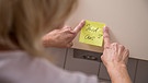 Eine Frau klebt einen Zettel zur Erinnerung in die Küche | Bild: picture alliance / dpa Themendienst | Christin Klose