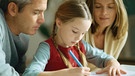 Eltern schauen ihrer Tochter beim Schreiben über die Schulter | Bild: colourbox.com