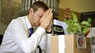 Mann sitzt erschöpft vor Schreibtisch mit gepackter Kiste | Bild: picture-alliance/dpa