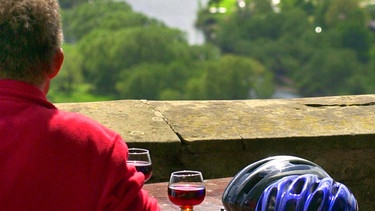 Ein Mann sitzt im Garten des Ausflugslokales der Vogelsburg bei Volkach und genießt bei einem Glas Rotwein die Aussicht auf die Mainschleife bei Escherndorf | Bild: picture-alliance/dpa