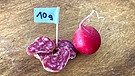 Ein paar Scheibchen Salami, ein Schildchen mit der Auftrag 10 g und ein Radieschen: Ernährung | Bild: BR/Christine Schneider