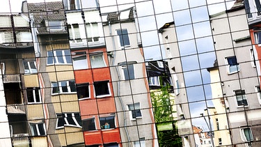 Wohnhäuser spiegeln sich in einer modernen Glasfassade. | Bild: picture alliance/dpa/Geisler-Fotopress/Christoph Hardt