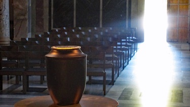 Urne, die in einem lichtdurchfluteten Kirchenraum aufgestellt ist | Bild: BR/Gesche Piening