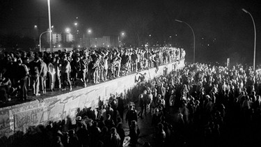 Fall der Berliner Mauer: In der Nacht des 9. November 1989 sind Menschen auf die Mauer am Brandenburger Tor geklettert. | Bild: pricture alliance/imageBROKER/Norbert Michalke