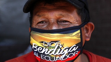 Mann aus Ecuador, der einen Mundschutz trägt mit der Aufschrift "Gott segne Ecuador". | Bild: picture alliance/Juan Diego Montenegro/dpa