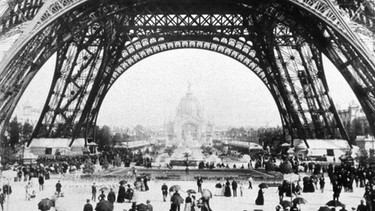 Ausstellungsbesucher wandeln unter dem Eiffelturm, die Sensation der Weltausstellung in Paris 1889 | Bild: picture-alliance/dpa