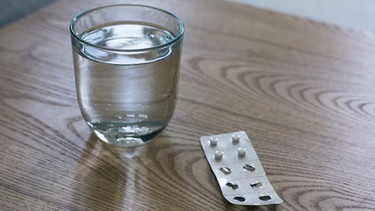 Ein Glas Wasser mit Tabletten in Blisterverpackung. | Bild: BR/Lisa Hinder