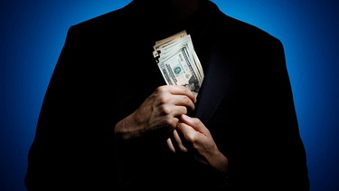 Silhouette eines Mannes vor blauem Licht, der sich ein Bündel Geldscheine in das Sakko steckt. | Bild: picture alliance / photothek | Thomas Trutschel