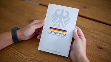 Eine Frau hält das Grundgesetz, GG, der Bundesrepublik Deutschland, in den Händen. | Bild: picture alliance / Fotostand | Fotostand / K. Schmitt
