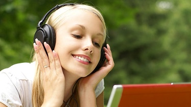 Frau mit Kopfhörern und Laptop in der Wiese lächelt | Bild: colourbox.com