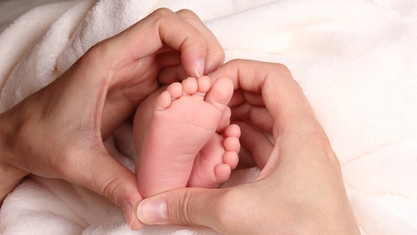 Mütterliche zu einem Herz geformte Hände umfassen Babyfüße | Bild: picture-alliance/dpa