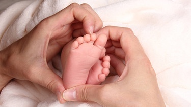 Mütterliche zu einem Herz geformte Hände umfassen Babyfüße | Bild: picture-alliance/dpa