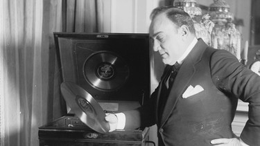 Enrico Caruso hält eine Schallplatte in der Hand. | Bild: picture alliance / ZUMAPRESS.com | BuyEnlarge