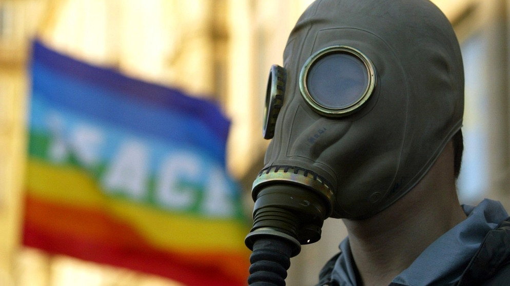 Demonstrant mit Gasmaske, im Hintergrund eine Regenbogenfahne mit der Aufschrift "Pace" (Italienisch für Frieden).  | Bild: picture-alliance/dpa