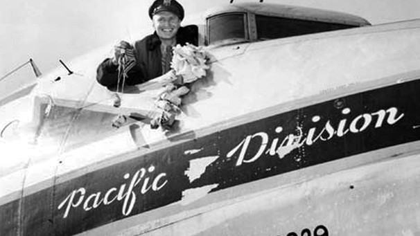 Mann in Flugzeug mit Schriftzug "Pacific Division" zeigt lächelnd Süßigkeiten | Bild: picture-alliance/dpa