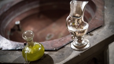 Am Rande eines Taufbeckens stehen eine Wasserkaraffe und Chrisamöl in einem Glasflakon bereit | Bild: picture-alliance/dpa