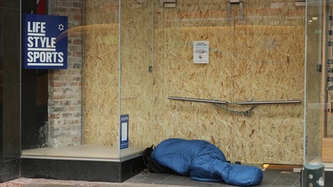 Ein Obdachloser schläft im Eingang eines geschlossenen und mit Brettern vernagelten Geschäfts | Bild: BR/NiallCarson