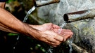 Hände fangen Wasser von einem Brunnen auf. | Bild: Colourbox.com/ Gelpi