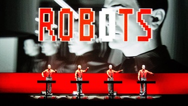 Band Kraftwerk auf der Bühne, die Leinwand zeigt den Schriftzug Robots | Bild: picture-alliance/dpa