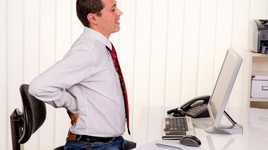 Mann sitzt am Computer und hält sich den schmerzenden Rücken | Bild: colourbox.com