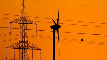 Strommast und Windrad vor orangem Himmel. Ist Strom besser als Wasserkraft? | Bild: picture-alliance/dpa