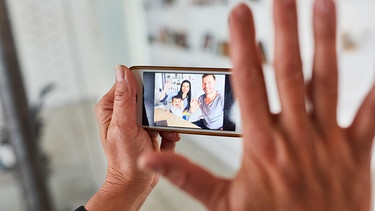 Hand hält ein Smartphone im Video Streaming mit einer Familie mit Kind | Bild: picture alliance / Zoonar | Robert Kneschke