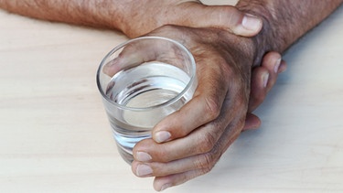 Zitternde Hände halten ein Glas Wasser. | Bild: colourbox.com/Astrid Gast