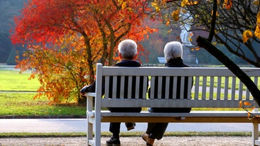 Zwei Senioren sitzen im Herbst im Park auf einer Parkbank. | Bild: stock.adobe.com/farbkombinat