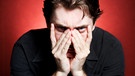 Mann im schwarzen Hemd mit Händen vorm Gesicht blickt angstvoll in die Kamera | Bild: colourbox.com