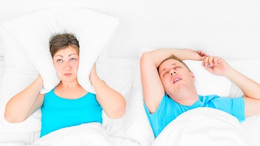 Mann und Frau liegen im Bett, Frau hält sich mit Kissen Ohren zu, weil der Mann schnarcht | Bild: colourbox.com