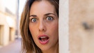 Eine Frau sieht mit offenem Mund hinter einer Mauer hervor. | Bild: picture alliance / Westend61 | VITTA GALLERY