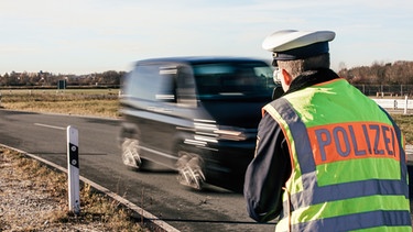 Ein Polizist der Münchner Polizei misst an einer Landstraße mit Hilfe eines Geschwindigkeitsmessgerät die Geschwindigkeit entgegen kommender Fahrzeuge. | Bild: BR/Fabian Stoffers 